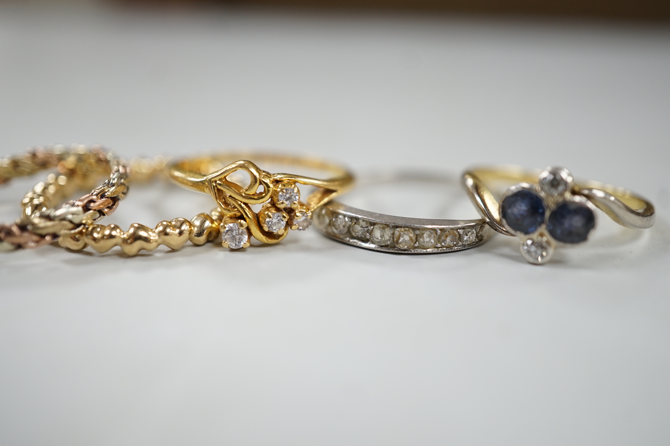 Three assorted white or yellow metal and gem set rings, including sapphire and diamond four stone cross over ring and a graduated diamond chip set half eternity ring, a similar three colour band, gross weight 8 grams and